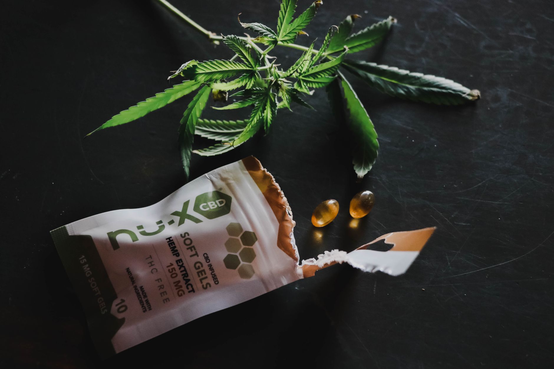 Capsules de CBD renversées à côté d'un emballage ouvert et d'une feuille de chanvre